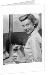 1950s Smiling Blonds Woman Mother Warming A Baby Bottle Of Milk In Kitchen Looking At Camera by Anonymous
