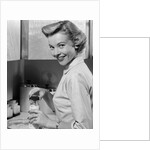 1950s Smiling Blonds Woman Mother Warming A Baby Bottle Of Milk In Kitchen Looking At Camera by Anonymous