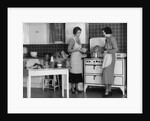 1930s Woman Housewife And Friend Wearing Apron Cooking Food In Kitchen On Gas Stove Indoor by Anonymous