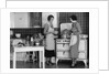 1930s Woman Housewife And Friend Wearing Apron Cooking Food In Kitchen On Gas Stove Indoor by Anonymous
