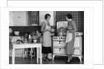 1930s Woman Housewife And Friend Wearing Apron Cooking Food In Kitchen On Gas Stove Indoor by Anonymous