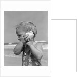 1950s Blond Toddler Girl Listening To Ocean In A Seashell Wearing Teddy Bear Bathing Suit by Anonymous