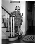 1950s Teenage Girl In Plaid Dress And White Ankle Socks On Stairway Holding Banister Carrying School Books Looking At Camera by Anonymous