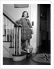 1950s Teenage Girl In Plaid Dress And White Ankle Socks On Stairway Holding Banister Carrying School Books Looking At Camera by Anonymous