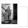 1950s Teenage Girl In Plaid Dress And White Ankle Socks On Stairway Holding Banister Carrying School Books Looking At Camera by Anonymous