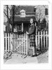 1940s Smiling Pretty Young Teenage Girl Standing By White Picket Fence In Front Of Stone House In Autumn Looking At Camera by Anonymous