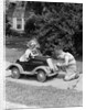 1940s 1930s Boy On Sidewalk Fixing Headlight Of Toy Car Driven By Little Girl Playing Outdoor by Anonymous
