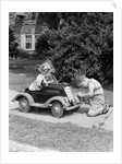 1940s 1930s Boy On Sidewalk Fixing Headlight Of Toy Car Driven By Little Girl Playing Outdoor by Anonymous