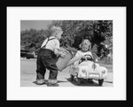 1950s Little Boy Playing Gas Station Pouring Water Into Toy Car For Little Girl by Anonymous