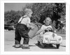 1950s Little Boy Playing Gas Station Pouring Water Into Toy Car For Little Girl by Anonymous