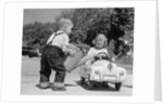 1950s Little Boy Playing Gas Station Pouring Water Into Toy Car For Little Girl by Anonymous