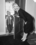1950s Blonde Mom Opening Front Door To Let In Child Dressed Winter Snow Suit Scarf Hat Can See Snow Scene Through Door by Anonymous