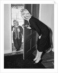 1950s Blonde Mom Opening Front Door To Let In Child Dressed Winter Snow Suit Scarf Hat Can See Snow Scene Through Door by Anonymous