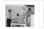 1940s housewife in kitchen showing plucked turkey to children by Anonymous