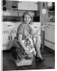 1960s smiling housewife sitting on full laundry basket by Anonymous