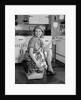 1960s smiling housewife sitting on full laundry basket by Anonymous
