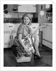 1960s smiling housewife sitting on full laundry basket by Anonymous