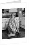 1960s smiling housewife sitting on full laundry basket by Anonymous