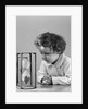 1940s young girl leaning on table staring at hourglass by Anonymous
