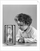 1940s young girl leaning on table staring at hourglass by Anonymous