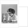 1940s young girl leaning on table staring at hourglass by Anonymous