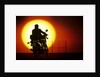 1980s silhouette of anonymous man on motorcycle driving toward rising setting sun by Anonymous