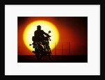 1980s silhouette of anonymous man on motorcycle driving toward rising setting sun by Anonymous