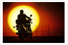 1980s silhouette of anonymous man on motorcycle driving toward rising setting sun by Anonymous