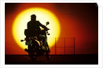 1980s silhouette of anonymous man on motorcycle driving toward rising setting sun by Anonymous