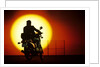 1980s silhouette of anonymous man on motorcycle driving toward rising setting sun by Anonymous