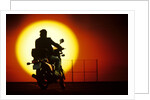 1980s silhouette of anonymous man on motorcycle driving toward rising setting sun by Anonymous