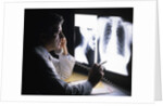 1980s doctor looking at x-ray while speaking on telephone by Anonymous