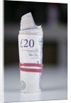 A roll of twenty pound notes on a table by Anonymous