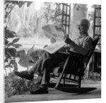 1970s elderly man reading newspaper on porch in a rocker by Anonymous