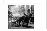 1970s elderly man reading newspaper on porch in a rocker by Anonymous