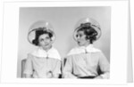 1960s two women sitting under hairdryers gossiping by Anonymous