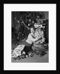 1950s portrait of young woman holding stack of presents next to a Christmas tree by Anonymous