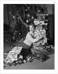 1950s portrait of young woman holding stack of presents next to a Christmas tree by Anonymous