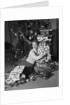 1950s portrait of young woman holding stack of presents next to a Christmas tree by Anonymous