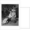 1950s portrait of young woman holding stack of presents next to a Christmas tree by Anonymous
