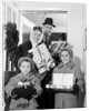 1960s family standing in doorway wearing winter coats and holding Christmas presents by Anonymous