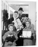 1960s family standing in doorway wearing winter coats and holding Christmas presents by Anonymous