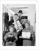 1960s family standing in doorway wearing winter coats and holding Christmas presents by Anonymous