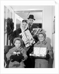 1960s family standing in doorway wearing winter coats and holding Christmas presents by Anonymous