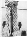 Woman holds on large Northern Pike on a lake pier, ca. 1950. by Anonymous