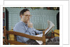 Pensive Man Reading Newspaper in Living Room by Anonymous