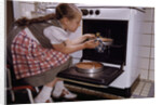 Girl Wearing Apron Removing Cakes from Oven by Anonymous