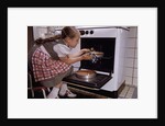 Girl Wearing Apron Removing Cakes from Oven by Anonymous