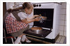 Girl Wearing Apron Removing Cakes from Oven by Anonymous