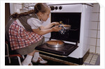 Girl Wearing Apron Removing Cakes from Oven by Anonymous